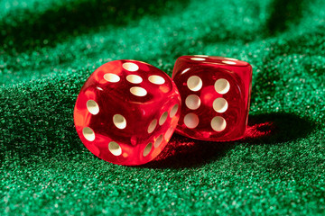 Red acrylic transparent dices for games. Two gambling translucent dices on green velvet surface, close-up.