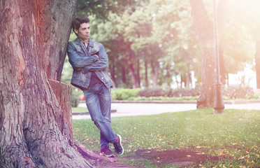 Naklejka premium A young man walks in the park at lunch time. A man is on a walk in the city. A student in the park.