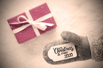 Label With English Calligraphy Merry Christmas And A Happy 2020. Gray Glove With Pink Gift And Snow Background And Snowflakes