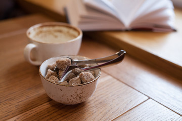 Sugar bowl with brown sugar on a light wood table. Cozy cafe, hygge concept, close-up