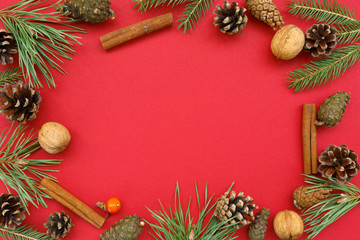 Beautiful background with frame and copy space for your text for Christmas holiday. Pine branch, cones, cinnamon and nuts on the red background. 