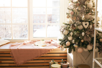 Style, interior design and creative ideas concept. Indoor view of large window at daylight with warm blanket and mug on windowsill, beautiful new year's tree decorated with white baubles and toys
