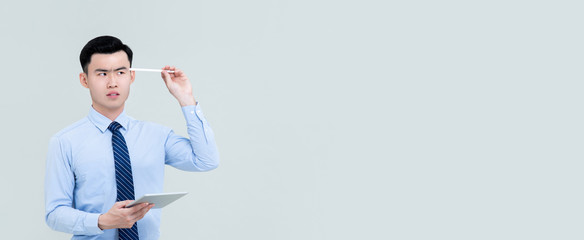 Young thoughtful Asian professional man holding stylus to head beside copy space