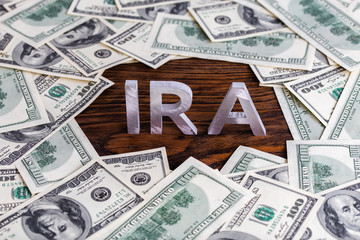 the word ira made of silver metal letters on wooden background surrounded by us dollar banknotes