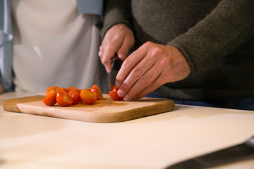 Cose-up of male hands cutting tomatoes in a kitchen on a wooden cutting board.