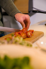 Cose-up of male hands cutting tomatoes in a kitchen on a wooden cutting board.