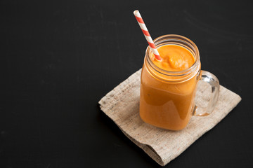 Homemade pumpkin smoothie in a glass jar mug over black background, low angle view. Copy space.