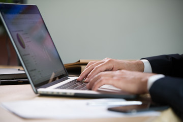 Close-up of male hands typing on a laptop in an office setting