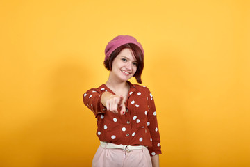 Beautiful caucasian lady points finger at you with a confident expression wearing pretty red shirt with polka dot on isolated yellow background