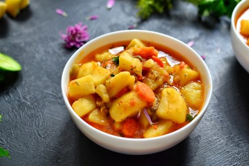Vegetable stew in a white bowl. Photo food. Stew with potatoes and carrots on a dark concrete background. Healthy vegetarian food.