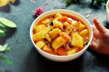 Photo of food on a dark background. Children's hands and food. The child holds hands a bowl with vegetable stew. Baby is having lunch. Food on a concrete background.