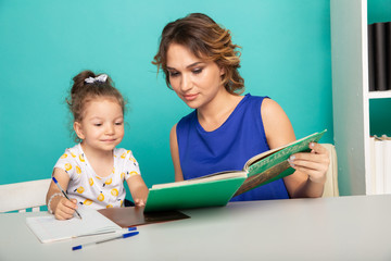 Pretty mother with cute daughter sitting with book in the room at home