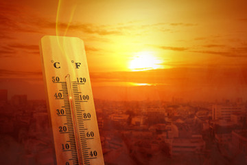Thermometer with high temperature on the city with glowing sun background