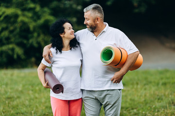 Fototapeta premium Happy senior woman and man standing outdoor and holding a yoga mat and looking each other- Concept sport - Image