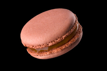 Macro photo of french caramel macaroon or macaron isolated on black background