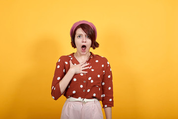Beautiful caucasian young funny woman wearing pretty red shirt with polka dot surprised and shocked while looking right on isolated yellow background