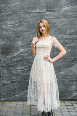 Young woman in evening dress posing on city street, dark wall background