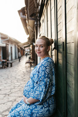 Portrait of beautiful pregnant woman. She is standing in the middle of the street and holding hands on her belly. 