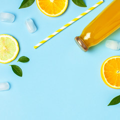 Flat lay composition with glass bottles of juice or fresh, slices of fresh lemon and orange, green leaves, ice cubes on blue background top view copy space. Citrus Juice Concept, Vitamin C, Fruits