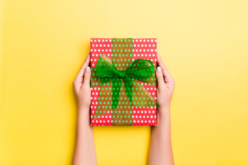 Woman arms holding gift box with colored ribbon on yellow table background, top view and copy space for you design