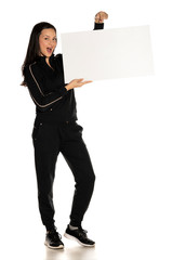 Young smiling woman in black track suit holding empty white board on white background