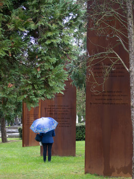 woman with umbrella next to three iron columns in Derio, Bizkaia