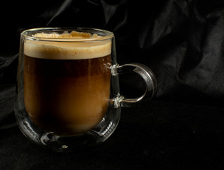 A transparent mug of coffee with milk and foam