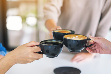 Closeup image of people enjoyed drinking and clinking coffee cups on the table in cafe