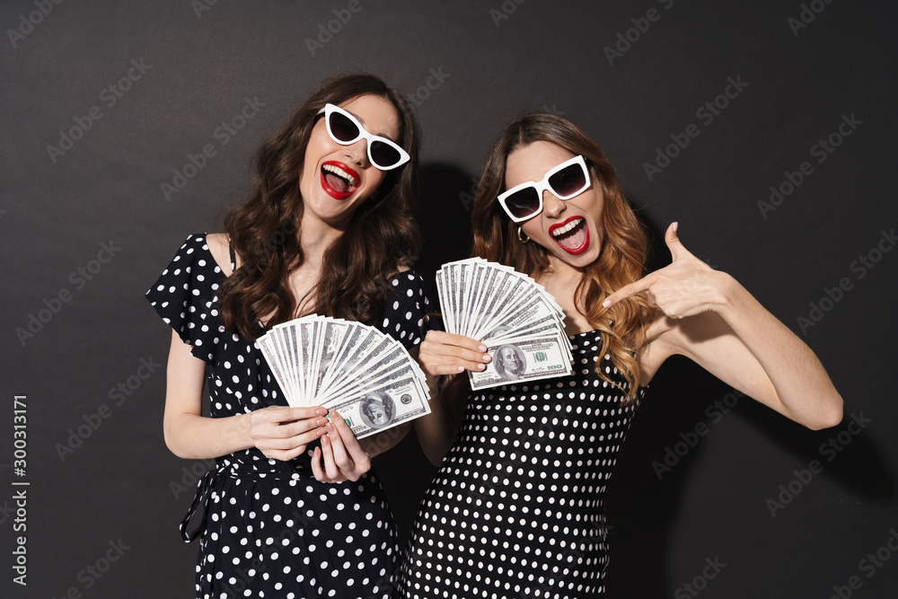 Sticker Portrait of two excited women holding and pointing finger at dollars