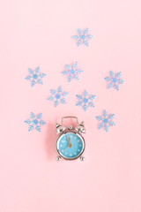Christmas background. Retro alarm clock blue, blue snowflakes on pastel pink background top view. flat lay