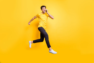 I'm on my way darling. Full body photo of handsome guy jumping high talking telephone rushing romantic date wear casual t-shirt trousers isolated yellow color background