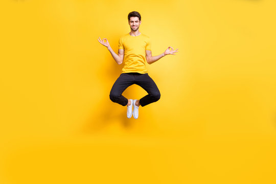 Full body photo of handsome guy jumping high lotus position morning yoga training relaxing fingers together wear casual t-shirt black trousers isolated yellow color background