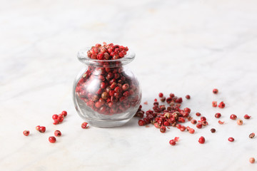 glass jar full of pink pepper grains rest on a marble table with copy space for your text