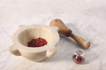 mortar and pestle with pink pepper grains rest on a marble table with copy space for your text