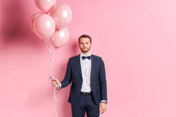 Sad male wearing formal suit hold pink balloons isolated over pink background. Sad emotions and...