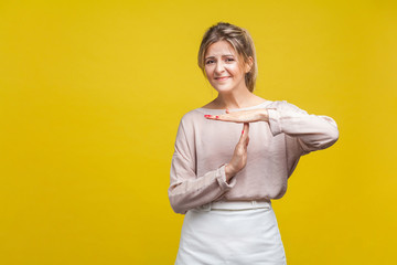 I need more time. Portrait of tired upset young woman with fair hair in casual beige blouse standing showing timeout gesture, looking at camera asking. indoor studio shot isolated on yellow background