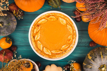 Autumn thanksgiving moody background with pumpkin pie, different pumpkins, fall fruit and flowers on green rustic wooden table. Flat lay