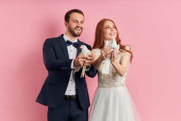 Charming lady and bearded caucasian man in tuxedo let pigeon out of hands, symbol of happy family life. Love, couple, relationships concept