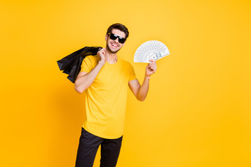 I will pay for it. Photo of handsome guy holding boutique bags making abroad shopping showing fan of usa bucks wear casual t-shirt pants isolated yellow color background