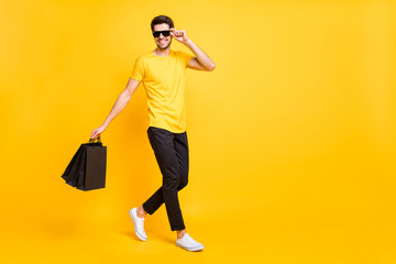 Full body profile photo of handsome guy carry boutique bags abroad shopping go fashionable mall wear casual t-shirt black pants isolated yellow color background