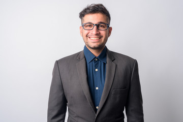 Portrait of happy young Persian businessman in suit with eyeglasses smiling
