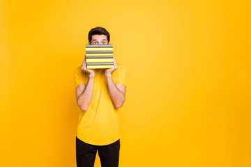 Portrait of his he nice attractive lovely funny brunette guy holding in hands hiding behind pile of book isolated over bright vivid shine vibrant yellow color background