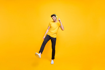 Fototapeta na wymiar Full length photo of handsome guy at students party listening youth music earflaps dancing youngster moves wear casual t-shirt pants isolated yellow color background