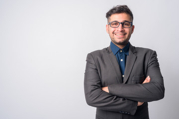 Portrait of happy young Persian businessman in suit smiling with arms crossed