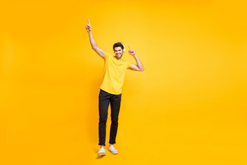 Full length body size photo of cheerful handsome attractive man wearing yellow t-shirt black trousers dancing with earphones worn isolated over vibrant color background