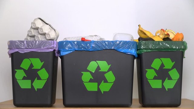 Distribution of waste for recycling at home. A woman's hand puts different types of garbage into different bins with a recycling sign