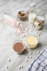 Zubereitung von heißer, dunkle und weiße Trinkschokolade mit Milch, Kakaopulver und Marshmellows auf Marmor hell Hintergrund 