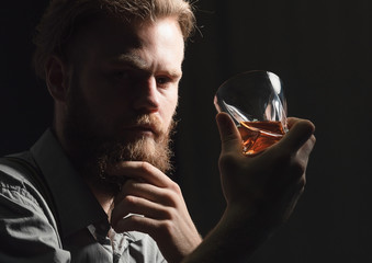 Portrait of a pensive handsome young man, with a glass of alcohol in his hands.