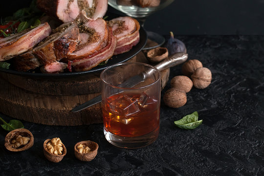A glass of whisky or brandy with a pork ham stuffed with walnuts and spinach wrapped in bacon. Meatloaf with nuts and herbs. Festive cuisine.