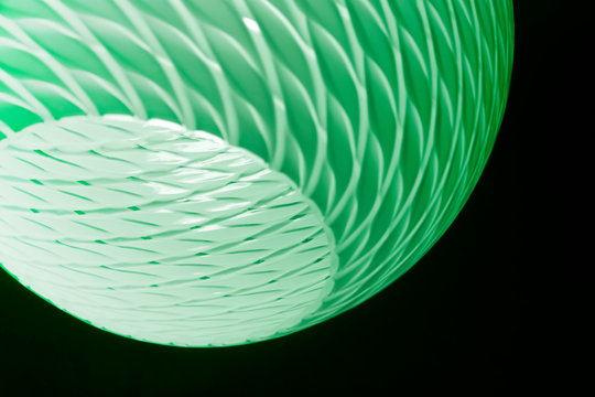 Toned photo of luminous lampshade in darkness. Close-up of lighting fixture. Abstract architecture detail. Glowing object with ripple pattern in concept of home interior and green technologies.